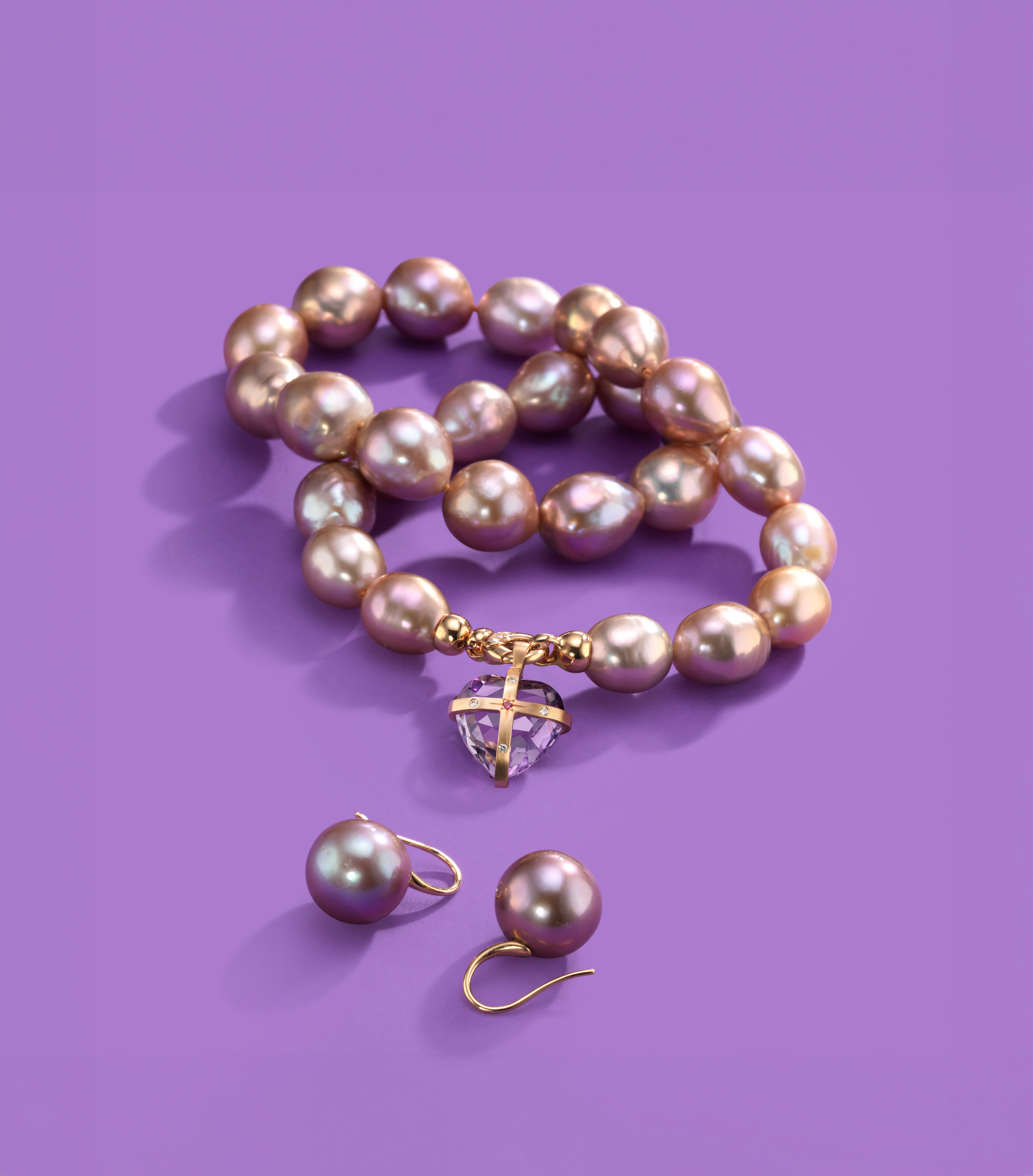 Violett schimmernde Perlenkette und Ohrringe auf violettem Hintergrund, mit goldenen Details