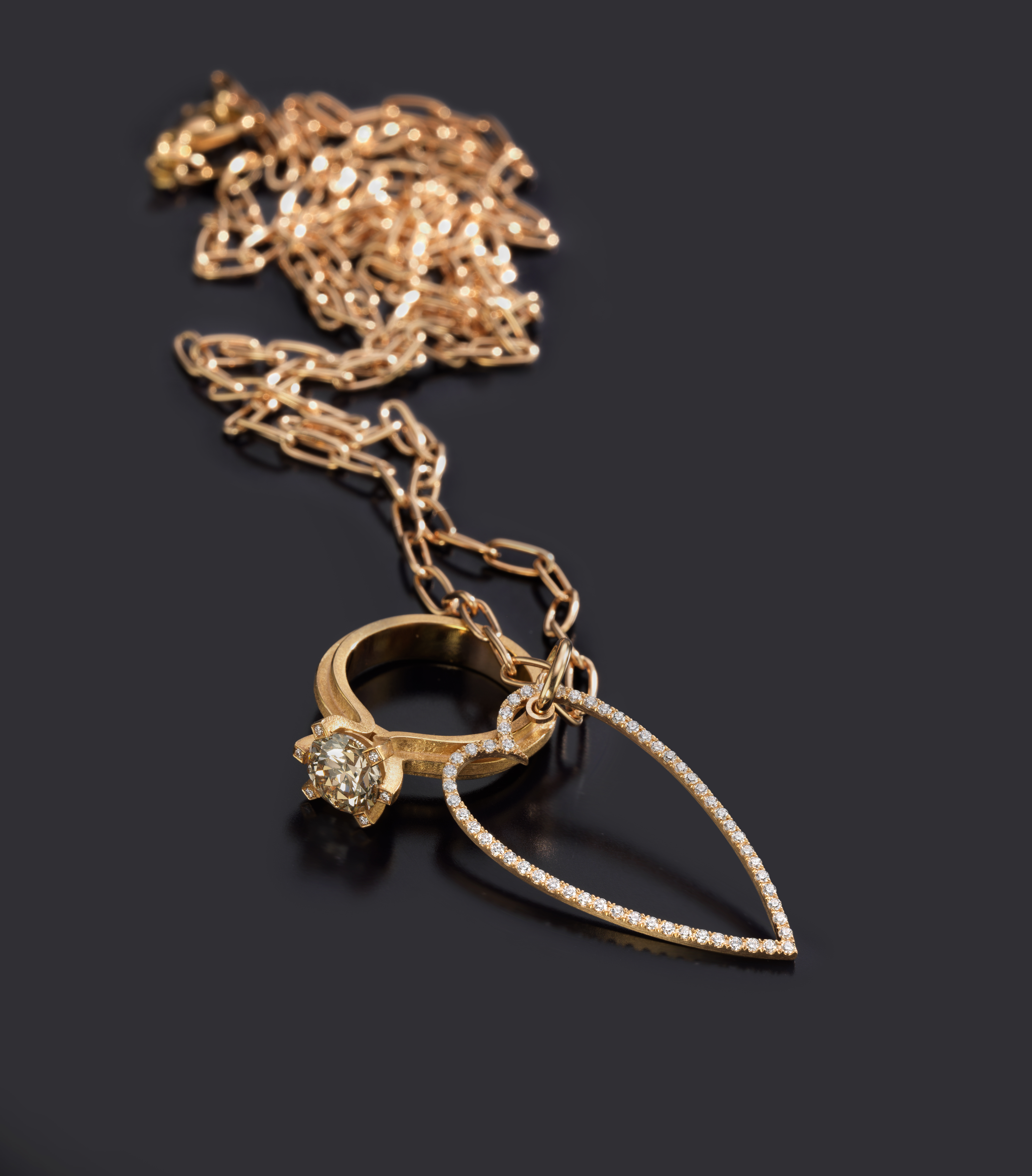Goldene Kette mit diamantbesetztem Herz-Anhänger und einem goldenen Ring, auf dunklem Hintergrund drapiert